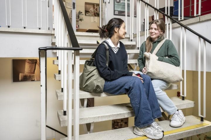 Twee studenten zitten op de trap in de hal van Verpleegschool Antwerpen.